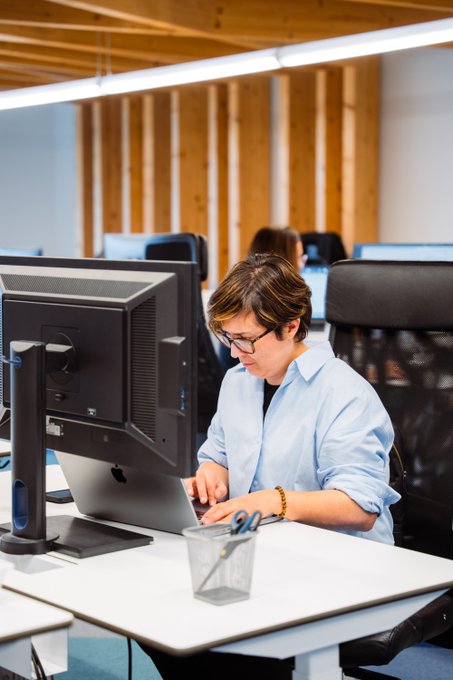 A focused professional in a light blue shirt and glasses types intently at a Dell computer in a modern office, with a small "xmoney.com" sign visible near the keyboard holder—visually reinforcing the post's message that deep concentration at the screen signals productive, high-quality work.
