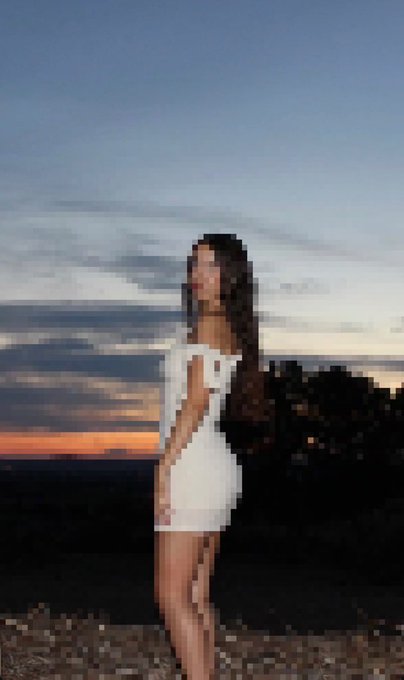 A pixelated image shows a woman with long dark hair wearing a short white dress, standing in profile against a sunset sky and distant landscape.