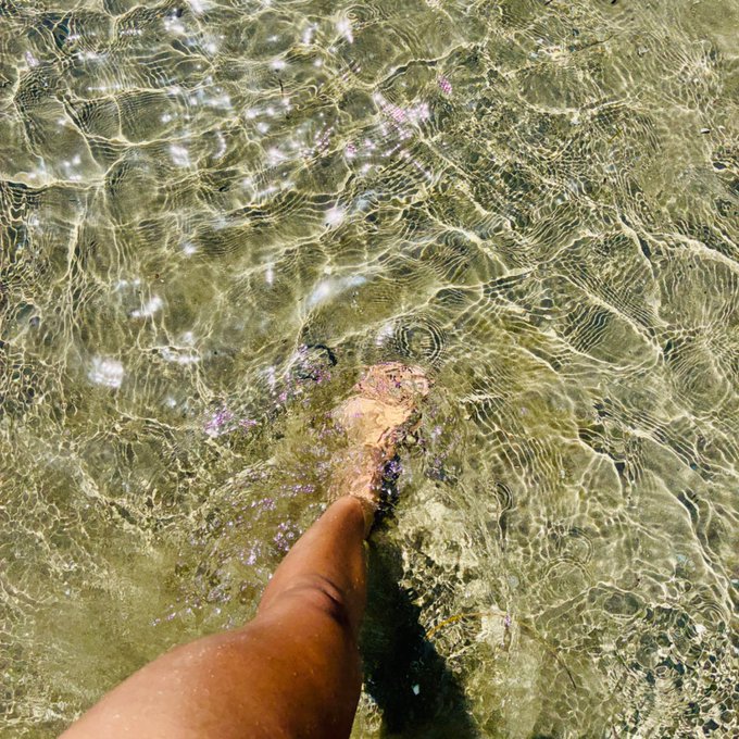 urn of water with ripples, reflecting the clear blue sky and green foliage above, as a person's foot sinks into it.