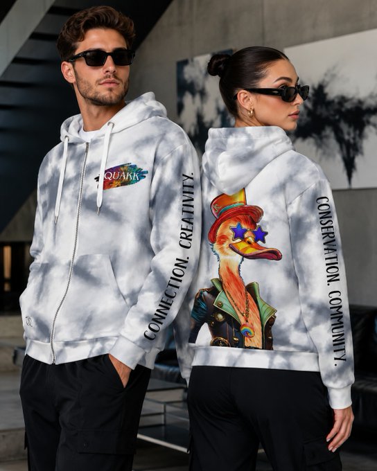 A man and woman model matching tie-dye hoodies featuring an 'aquark' logo with the text 'CONNECTION. CREATIVITY. CONSERVATION. COMMUNITY.' printed down the sleeves and a duck character wearing a top hat on the back.
