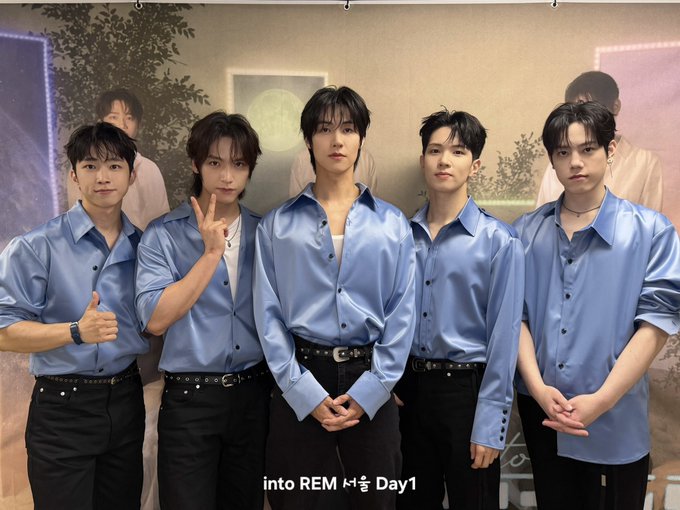 Five young men pose together in matching shiny blue button-up shirts and black pants during what appears to be a promotional event. The caption "into REM 서울 Day1" along with the post details "&CON5 into REM 260731~260802 서울" suggests this photo was taken on the first day of their Seoul concert event held from July 31 to August 2, 2026.