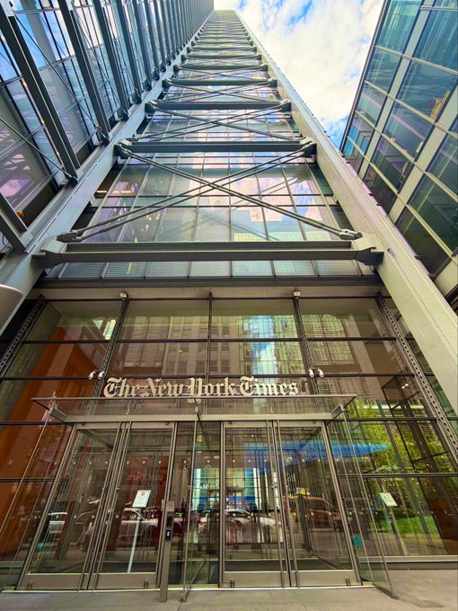 A low-angle shot of The New York Times building entrance, featuring its signature gold lettering on the glass facade.