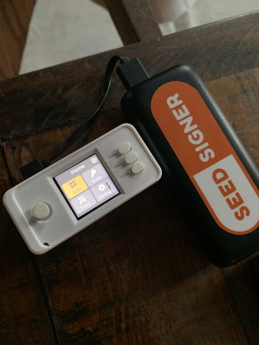A homemade SeedSigner device, an open-source Bitcoin hardware wallet, rests next to a "SEEDSIGNER" labeled power bank on a wooden surface, illustrating the DIY, open-source nature of the wallet in contrast to closed-source secure element hardware wallets.