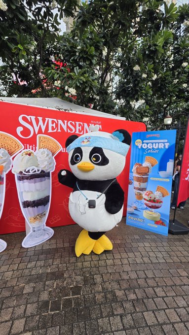A Swensen's mascot penguin wearing a headband and whistle stands cheerfully in front of a Swensen's promotional display featuring "Yogurt Series" ice cream products. The post connects to the image by highlighting a fan's excitement to try Swensen's new Luna-flavored ice cream, with the cute mascot adding to the fun promotional atmosphere.