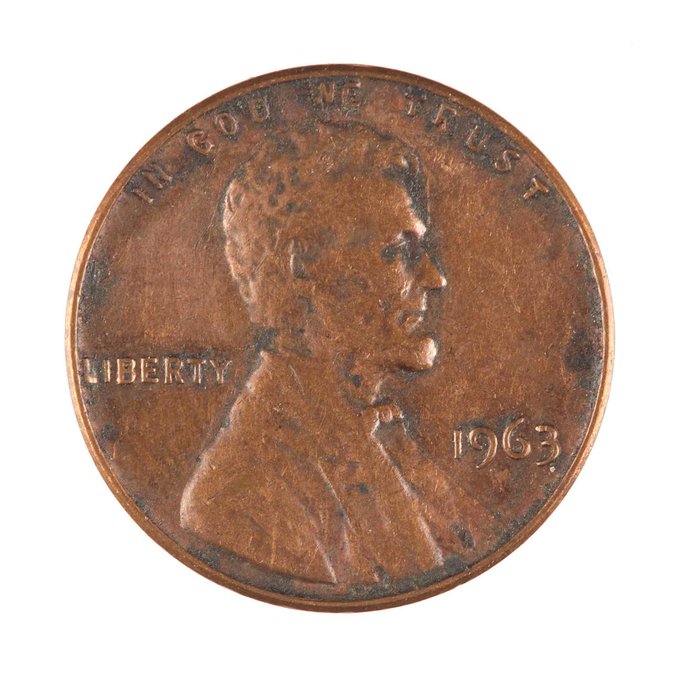 A close-up of a worn 1963 Lincoln penny with 'IN GOD WE TRUST' and 'LIBERTY' inscriptions, showing Abraham Lincoln's profile.