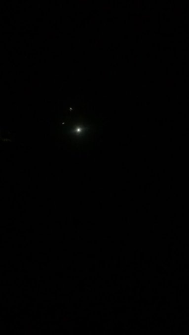 A mostly dark photograph showing only a small bright point of light in the center, possibly a distant light source or celestial object captured at night.