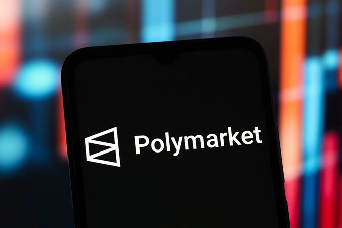 The image shows a black smartphone with the word "Polymarket" displayed on its screen. The phone is positioned at an angle, allowing for a clear view of the logo. The background features a colorful display that adds vibrancy to the scene.