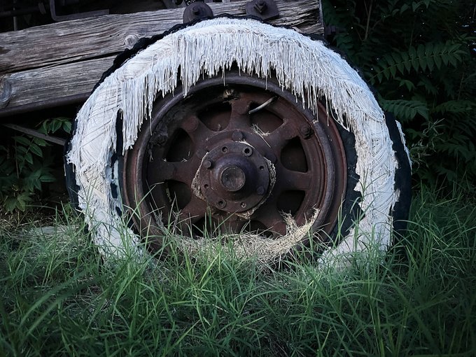 A weathered truck tire covered in long, dramatic icicles resting in tall green grass.