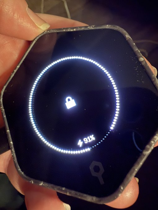 A hand holds a hexagonal Bitkey hardware wallet displaying a circular LED progress indicator at 91% with a padlock icon, suggesting a security setup or recovery process in progress. The image complements the post by visually capturing the "easy" onboarding experience the author describes—showing the sleek device mid-configuration as users adjust to a more user-friendly, emotionally reassuring approach to self-custody.