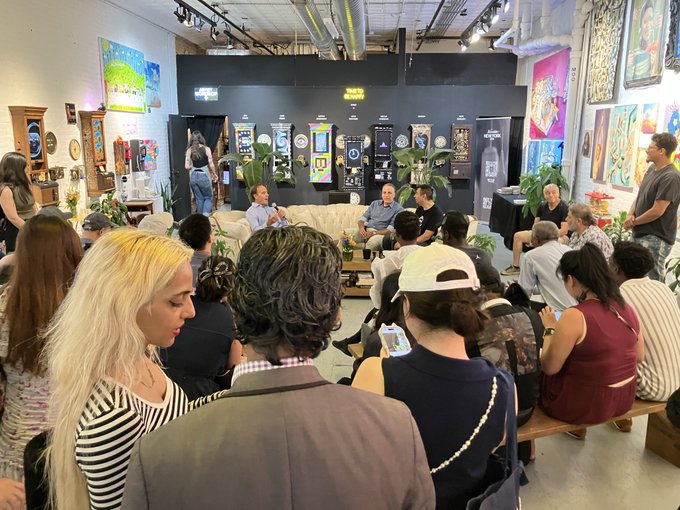 A crowd gathers at a panel-style event in an art-filled venue, with attendees seated on couches facing speakers at an art gallery in New York, as part of crypto community hangouts with Virtuals.io and CryptoMondaysNY at Solana Skyline.