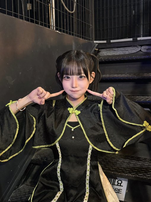 A young woman in an elegant black and gold traditional-style outfit with green accents playfully points to her cheeks while posing on metal stairs. The Korean hashtag "#루비뚜비시" (Rubytubbsi) suggests this is a fan photo featuring a cosplayer or performer, with the caption encouraging viewers to check out alternative content when they have time.