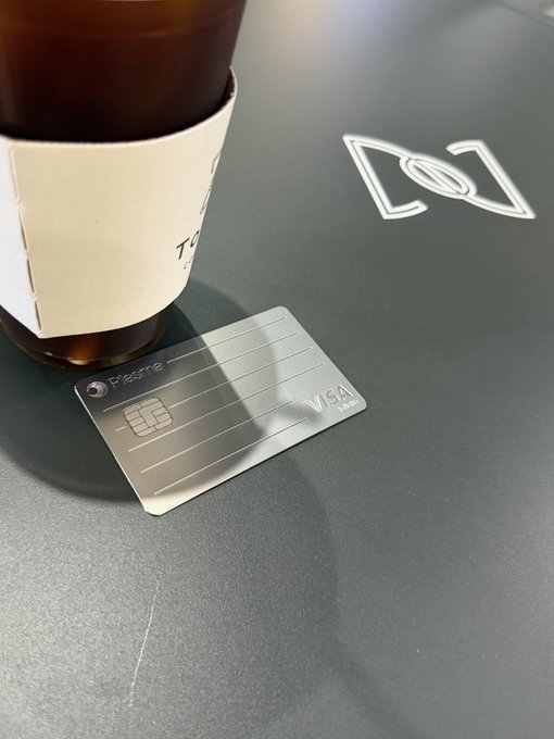 A physical Fipto-branded Visa debit card placed on a dark surface next to a glass bottle with a paper sleeve.