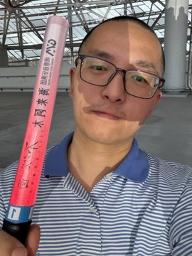 The image features a man wearing glasses, holding up a pink and white object that has Chinese writing on it. The man appears to be posing for a photo with this item as part of his background. The text "hold $BTW" is also present in the image.