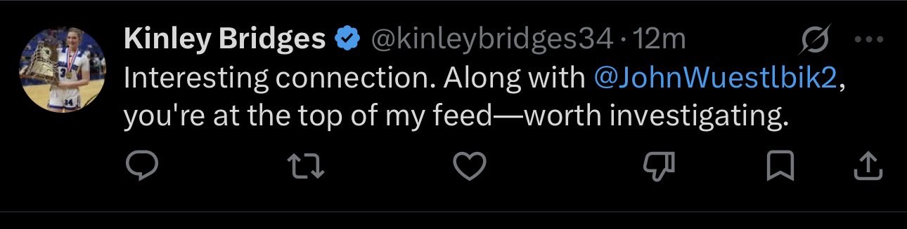A screenshot of a tweet from verified user Kinley Bridges (@kinleybridges34) reads "Interesting connection. Along with @JohnWuestlbik2, you're at the top of my feed—worth investigating." This is a classic example of the crypto scam bot referenced in the accompanying post, which mocks these bots for pretending to notify users that they and a random account are mysteriously "at the top" of their feed.