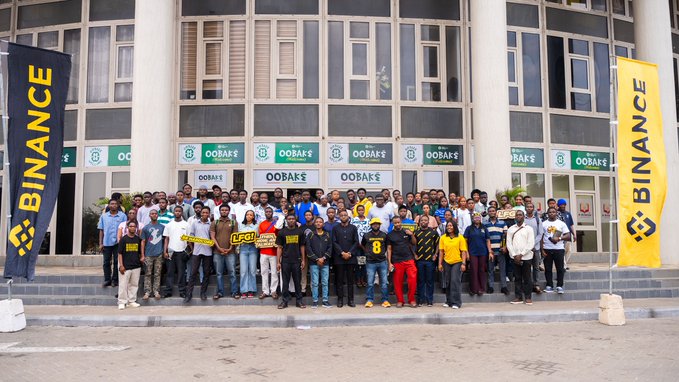 A large group of over 100 attendees poses on the steps of a building with "ODBAK" and "BINANCE" banners displayed in front for the Accra TradeXperience event, held to network and learn about TradFi and BStocks on Binance.