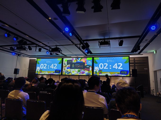 A conference audience sits facing three large screens displaying a countdown timer at '02:42' with 'Open Source Summit' and 'Tokyo' branding.