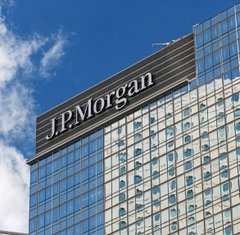 The image shows the JPMorgan corporate building featuring the prominent "JPMorgan" logo on its modern glass facade against a blue sky, visually representing the banking giant mentioned in the article about expanding its JPM Coin to the Ethereum network for 24/7 institutional payments.