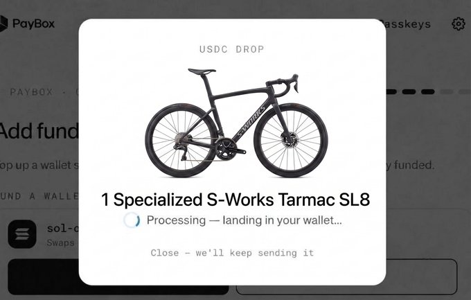 A Pop-Up window on PayBox shows a "USDC DROP" for 1 Specialized S-Works Tarmac SL8, with a status indicator reading "Processing — landing in your wallet…" The image illustrates the post's anecdote about the promo's rewards, showing a user receiving a high-value prize (worth thousands) in contrast to most participants who only claimed a few dollars.
