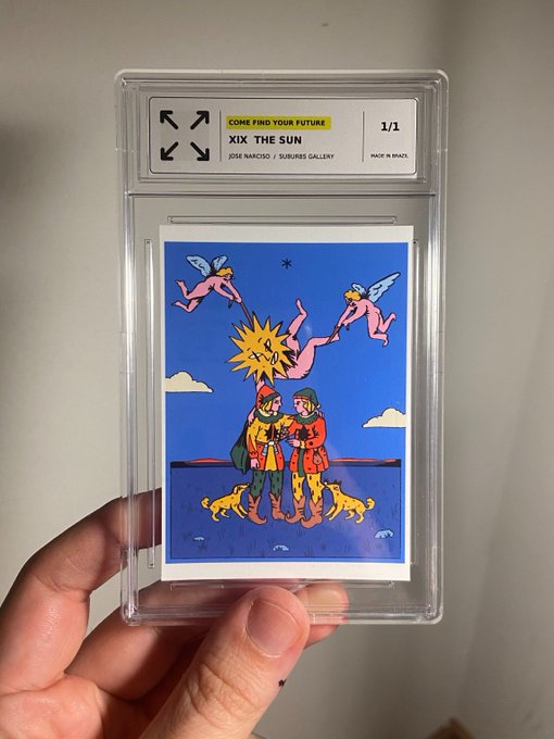 A hand holds a plastic-encased tarot card titled "XIX THE SUN" by Jose Narciso from Suburbia Gallery, featuring an illustrated scene with figures and cherubs against a blue background.