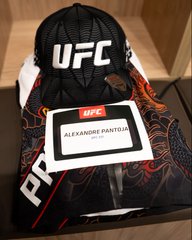 A black UFC-branded backpack with orange flame designs sits in a locker room, featuring a name tag that reads "Alexandre Pantoja" ahead of his upcoming title fight. The personalized gear signals his preparation for UFC331.