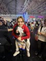 A young child stands in the foreground of a large indoor venue with arms outstretched, surrounded by people at what appears to be an indoor amusement park, jokingly presented as "Luna" carrying the heavy load of everyone around her through sheer presence.