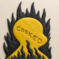 A graphic design or cutout featuring a yellow silhouette of a head surrounded by black flames, with the word "COOKED" written across the face.