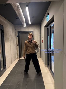 A full-body mirror reflection of a person posing in a hallway wearing a brown jacket and black pants, with overlaid text reading 'TODAY FEELING ROTA!! MAKE IT YOURSELF.'
