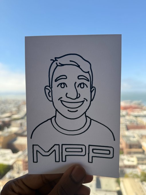 A hand holds up a piece of paper with a simple line drawing of a smiling man's face and the letters 'MPP' printed below, with a blurred cityscape visible in the background.