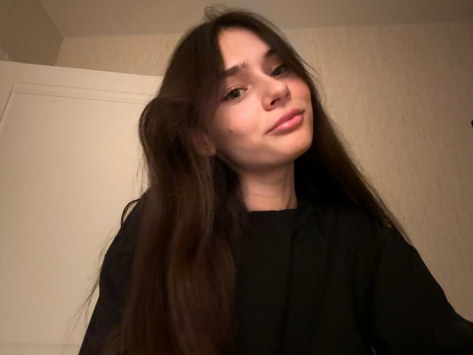A young woman with long dark hair wearing a black top takes a selfie indoors, posing for the camera in what appears to be a personal "GM" (good morning) greeting to the Polymarket community.