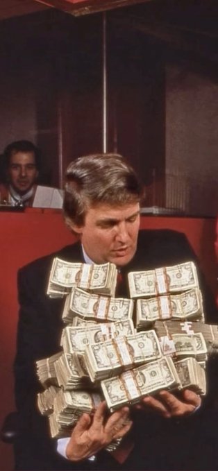 A retro-style photograph shows Donald Trump holding and looking at a large stack of bundled US dollar bills, with another person visible in the background.