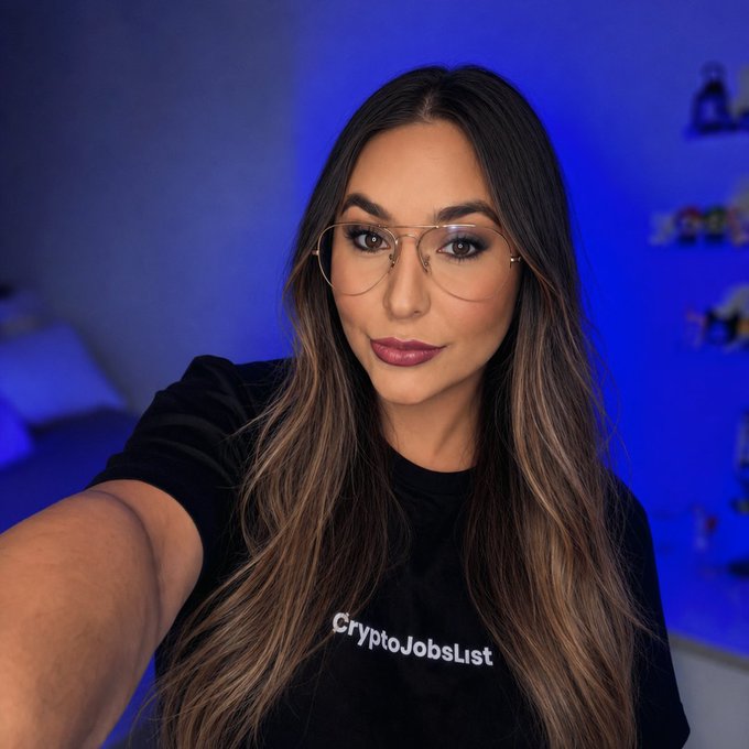 A woman wearing glasses and a black "CryptoJobsList" t-shirt takes a selfie with a blue-lit background, visually representing the brand behind the post highlighting 400+ open crypto, blockchain, and Web3 job opportunities across various roles.