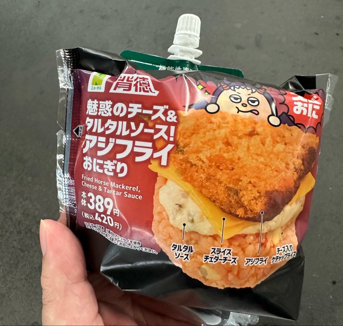 The image shows a hand holding a bag of food, which appears to be a type of sandwich or snack. The packaging for this food item features Japanese text that reads "Fried Fish & Chips. Cooked with Crispy Fried Fish, Crispy Fried Bread, and Crispy Fried Cheese". This suggests that the food is likely a type of fried fish sandwich or snack, as it contains ingredients like fried fish, bread, and cheese. The packaging also includes nutritional information in Japanese, which might provide details about the calorie content, fat content, protein content, and other important nutrients found in the food item.