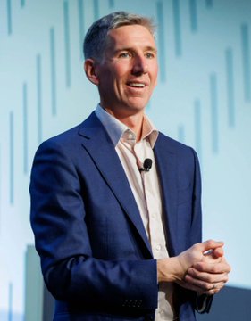 A man in a blue suit and white shirt speaks on stage with a microphone clipped to his lapel. The image likely relates to the post's claim about a Bitwise CIO predicting Bitcoin's price could reach $1.3 million by 2035 amid institutional investment.
