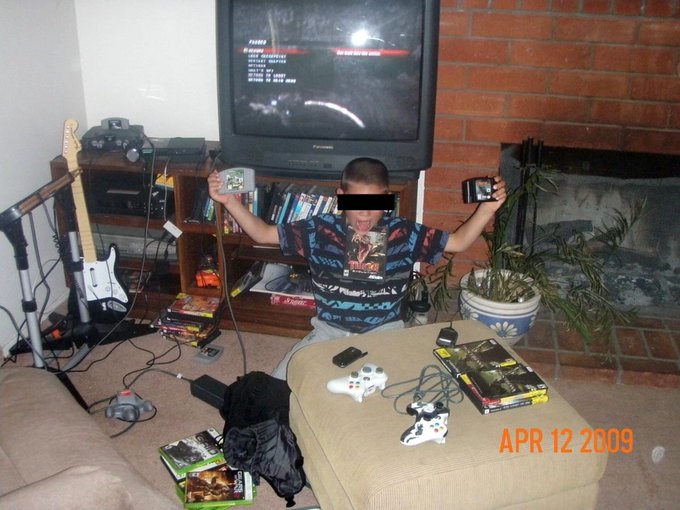 A nostalgic photo dated APR 12 2009 showing a person sitting on a couch in a living room holding up video game cases, surrounded by gaming equipment, guitars, and a TV displaying a game menu.