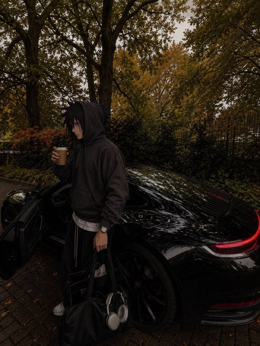 An anime-style character in a dark hoodie stands beside a black Porsche holding a coffee cup, with headphones and a bag.