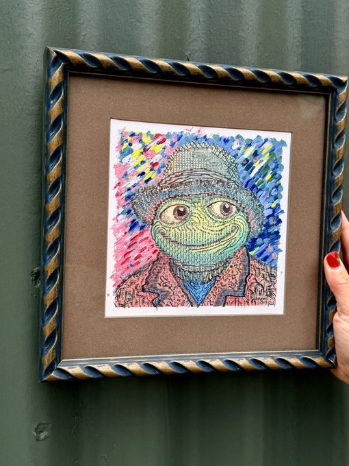 A framed colorful artwork depicting a green-faced figure in a knit cap, held against a green curtain by a hand with red nail polish.