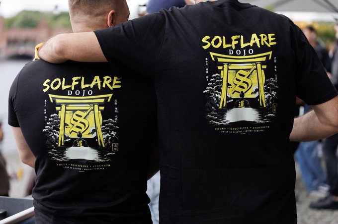 The image features two men wearing black t-shirts with yellow designs, including a yellow dragon and a yellow tree. One of the shirts has "solflare dojo" written on it, while the other shirt displays "Gm to all my homies on solana". The background shows people standing in front of a building, suggesting that they might be at an event or gathering related to the t-shirt designs.

The image also contains text elements such as "solflare dojo" and "Gm to all my homies on solana", which are likely part of the t-shirt designs or promotional materials for a specific event, product, or brand.