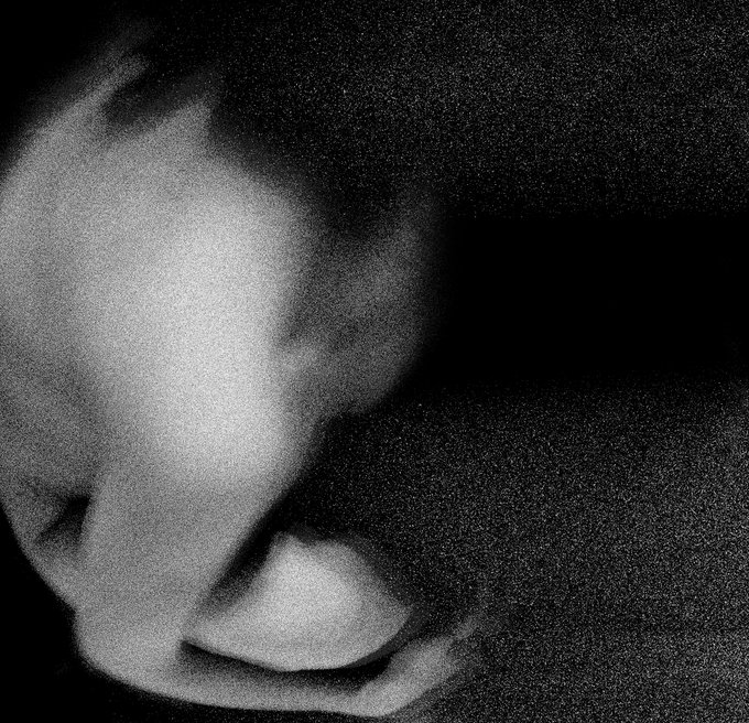 The image features a black and white photograph of a person's face, with their head turned to the left side of the frame. The background appears to be a dark area or shadow, which contrasts with the lighter areas around the person's face. The photo is titled "GM #TEZOSTUESDAY" in the caption below it.