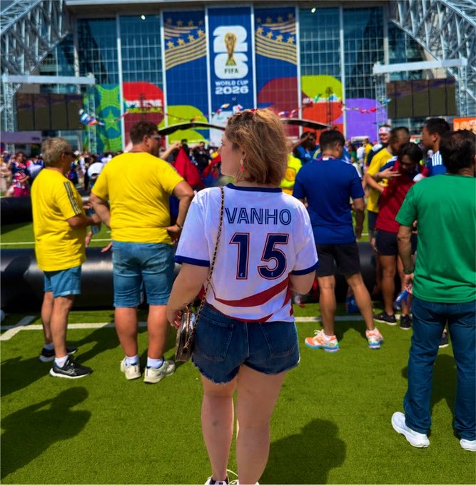 A person wearing a white jersey with 'VANHO' and the number '15' on the back stands in a crowd at what appears to be a FIFA World Cup 2026 fan event with various colorful national jerseys visible.