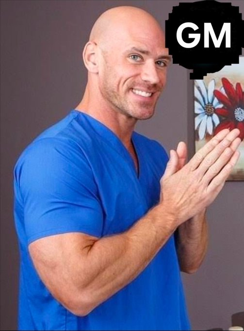A bald man in a blue t-shirt smiling and rubbing his hands together, with a black circular 'GM' logo in the top right corner.