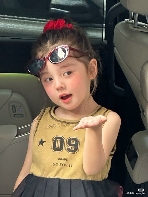 A young girl with a red scrunchie and pink sunglasses on her head blows a kiss toward the camera while sitting in a vehicle seat; text reads '小红书ID: Luyue_66'.