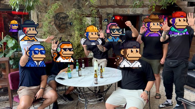 A group of people posing together outdoors at a restaurant table, with their faces obscured by various 8-bit style pixel art character stickers
