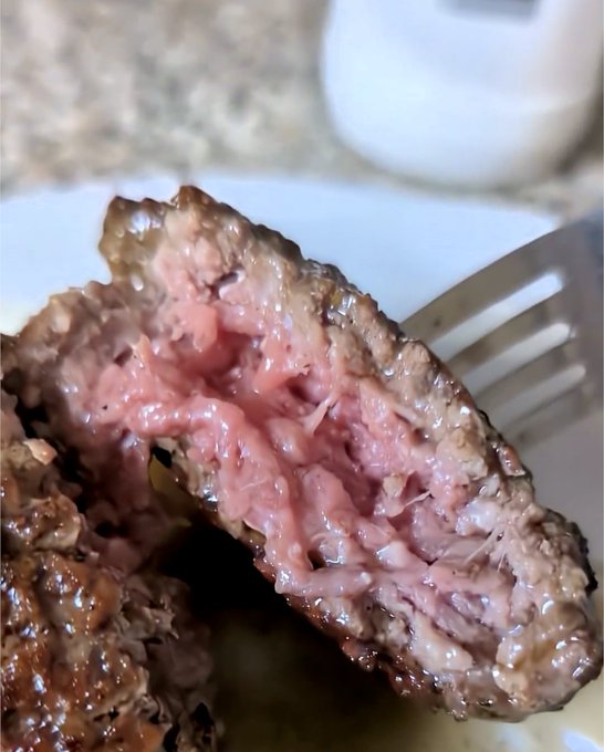 A close-up of a sliced piece of medium-rare steak on a fork, showing a pink, juicy interior with a seared brown crust.