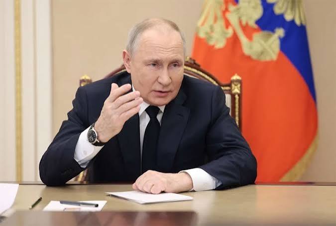 Russian President Vladimir Putin is pictured seated at a desk with the Russian flag in the background, an image used to illustrate news regarding his signing of new cryptocurrency regulation laws in Russia.