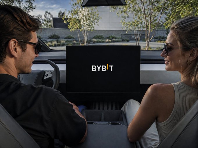 A man and woman wearing sunglasses sit inside a vehicle looking at each other, with a screen displaying the 'BYBIT' logo visible between them.