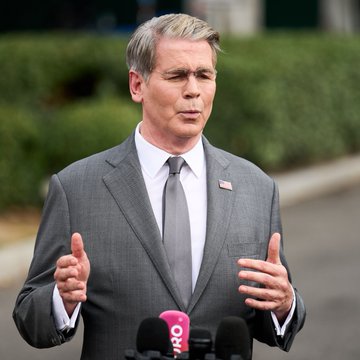 Scott Bessent, wearing a gray suit with an American flag pin, speaks to reporters with a microphone labeled "FOX" visible in the foreground, as he urges the Senate to advance the Clarity Act to maintain U.S. leadership in digital assets and national security.