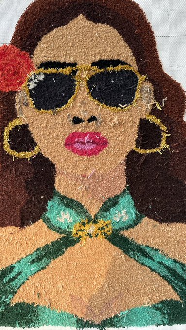 A textured, yarn-based portrait of a woman with brown hair, gold-rimmed sunglasses, large gold hoop earrings, and a green halter top, with a red flower in her hair.