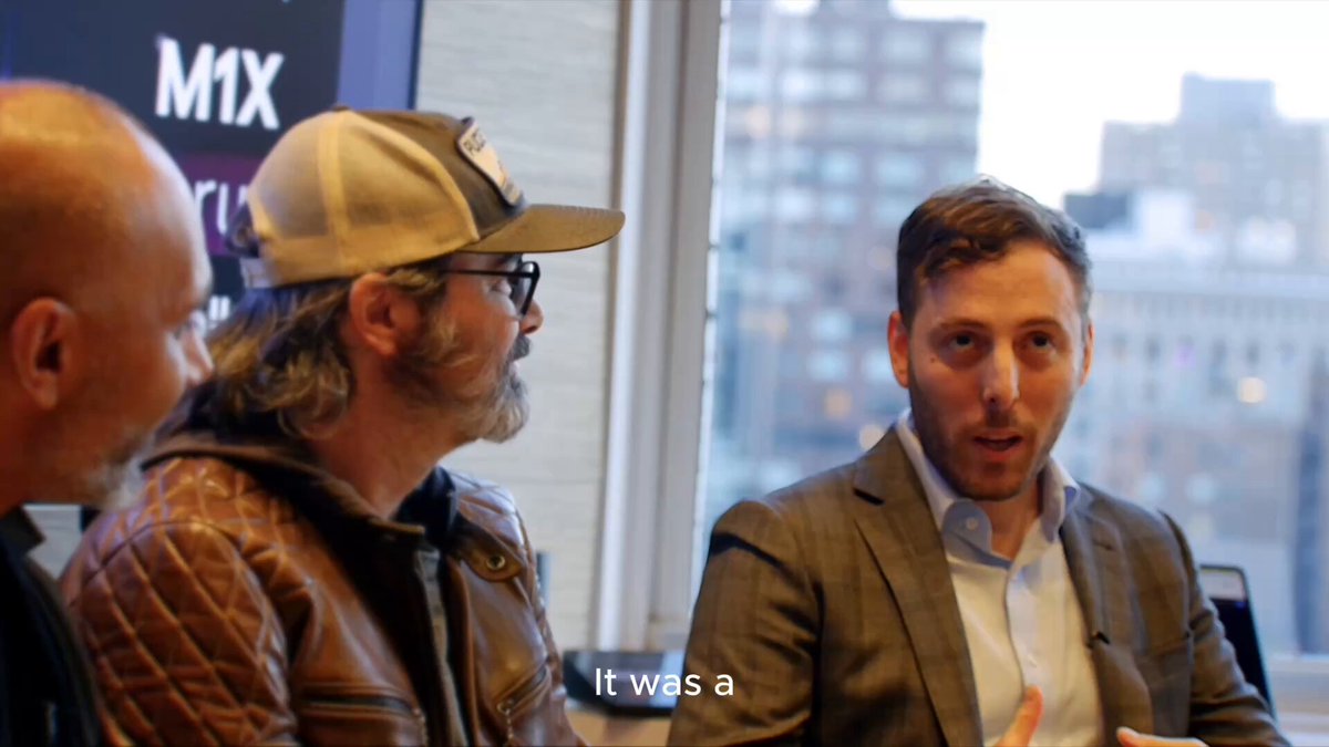 Three men are engaged in conversation at an event, with the "M1X" logo visible in the background and subtitles reading "It was a." The image captures a panel discussion, fitting the post's context of the Marshall Islands partnering with Stellar, as Mark Lurie (likely the speaker on the right) discusses the decision at The Stable Con.