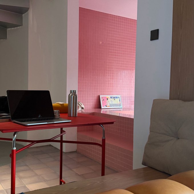A laptop and silver water bottle sit on a red table in a room featuring pink tiled walls and a small framed photo.