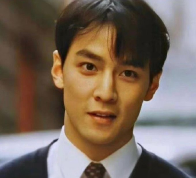 A young man with dark hair, wearing a white shirt, dark tie, and suit, looks directly at the camera in what appears to be a film still. The image's composed, cinematic portrait pairs with the caption "Let me reintroduce myself. My name is 0xMoon," lending a suave, dramatic flair to a personal reintroduction.